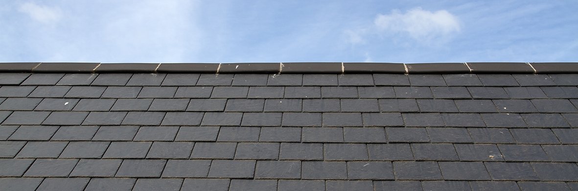 Professionally finished and installed slate tiles on a roof with blue sky